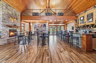 Great hall toward the porch doors: stone fireplace, loft, bar and wine wall. Digitally altered: fire added